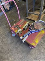 Overview of three metal wrenches, wood plane, and three tennis racquets on red and yellow cart.