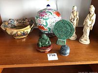 Wide view of Asian themed lot including Jade Buddha, decorative bowl, ginger jar, pair of figurines, circular decorative disc on stand.