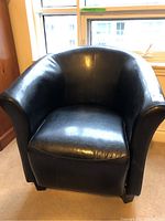 Front view of black leatherette barrel chair showing curved arms and cushioned seat.