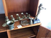 Five brass bird figurines on a single branch, a lady bell figurine, brass trivet, decorative cup, and a golfing trophy on a shelf.