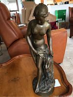 Front view of brass female nude statue on round base