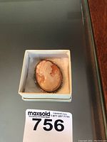 Front view of the oval cameo brooch showing the carved profile of a woman in peach and cream tones, set in a silver frame with decorative edges.