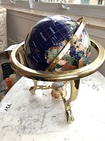 Side angle view of the blue globe on shiny brass tripod stand showing details of continents and meridian ring.