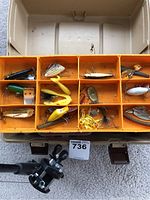 Opened plastic tackle box showing assortment of fishing lures including plugs, spoons, spinnerbaits, and soft plastics.