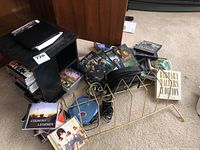 Overview of lot showing CDs, DVDs, black wooden shelf, wire record holder, and part of the iPod and cords.