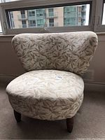 Front view of the bedroom chair showing leaf patterned beige and olive upholstery and cushioned seat.