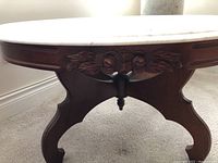 Close-up of the carved wood base showing floral and leaf designs beneath the marble top