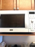 Front view of white Kenmore microwave showing large glass door, control panel with buttons and dial on right, and Kenmore branding.