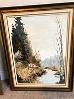 Oil painting in a gold wooden frame showing a fall forest with a stream and autumn colors.