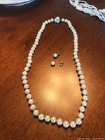 Single strand freshwater pearl necklace laid out with two pearl stud earrings on a wooden surface.