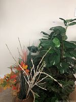 View of the large Monstera leaf artificial plant with visible wood pot and other plants behind it.
