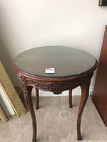 Full view of the round wooden table with detailed carved apron and legs, covered by a round glass top.