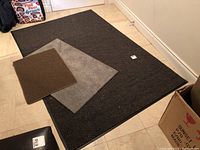 Set laid out on floor showing black large rug with rubber backing and two smaller mats on top, one gray and one brown. Normal wear visible.