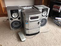 Full view of Sony audio system unit with two speakers and remote control on carpeted floor.