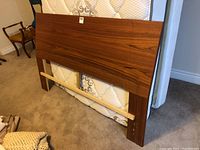 Full view of teak wood headboard leaning against a double mattress and other components, showing the size and minor wear