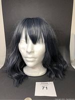 Front view of the wig on the white foam head stand showing layered bangs and wavy shades of blue and grey hair.