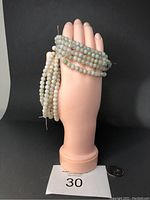 Photo showing multiple Burma jade stretch bracelets displayed on a hand-shaped stand. The bracelets are made of round jade beads in varying shades of light green and yellow.