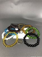 Photo showing ten stretch bracelets with crystal beads in various colors arranged in a circle with a quarter coin for size reference.