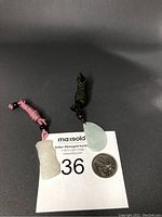 Two jade pendants with rope chain necklaces displayed on black background next to a quarter for size reference.