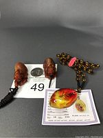 Three amber necklaces: one certified amber pendant with embedded leaf and certification card, two lab amber monster pendants on cords with amber colored beads.