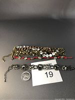 Top view of all three bracelets displayed, showing the bronze multi-chain bracelet with large Swarovski crystals, red coral and crystal bead bracelet, and the silver metal bracelet with black stones.