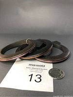 Three dark wooden bangles with glitter edges displayed with a coin and a lot number card for scale.