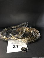 Three golden leaf patterned hair bands and bangle wrapped in plastic with a quarter for scale, against a black background.