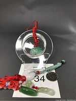 Four natural gemstone pendants displayed on a black surface with a coin for scale, showing red and green cord necklaces and carved jade pendants in various green and white tones.