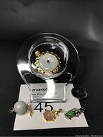 Lot of 4 pendants displayed on a clear round stand with a number 45 card and quarter for scale, showing Burma jade, pink agate, and green agate pendants.