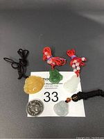 Four carved Buddha-shaped jade pendants in yellow, green, white, and pale blue colors with rope necklaces placed on a black background alongside a quarter for size reference.