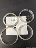 Four small natural agate bangles displayed on a dark surface with a coin for scale, showing clear to white translucent stone with natural patterning.