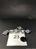 Six silver-tone engagement rings arranged in a row with a quarter coin for size reference, showing large central stones with smaller side stones, crystals and rhinestones.