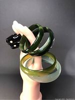 Six natural agate bangles on a hand mannequin showing varied green and translucent colors, multiple angles visible.