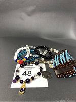The lot of seven stretch bracelets arranged around a quarter for size reference. Bracelets include amethyst with monster charm, turquoise multi-strand, clear crystal with enamel flower dangles, rose shell beads, and agate/crystal combinations.