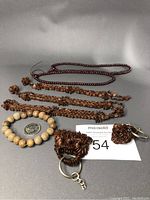 Overview of 8 items: 1 stretch bead bracelet in light tan, 3 various carved handmade bracelets, 2 prayer bead bracelets, and 2 carved keychains with metal rings and chains