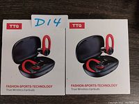 Front view of two unopened retail boxes of TTQ true wireless sport earbuds in black and red, each with charging case pictured on box.