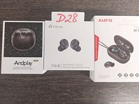 Three boxed sets of true wireless earbuds from Amdplay, Tranya, and AUFO displayed side by side.