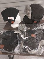 Four Bluetooth-enabled toques displayed on mannequin head and table including fleece-lined and fuzzy water-repellent styles with ear flaps and face mask.