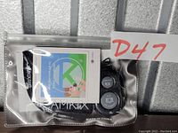 Clear plastic zip pouch containing the Bluetooth phone camera shutter remote, wrist strap, and user manual with brand name KAMKIX shown.