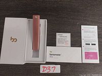 Femometer Vinca basal body thermometer in rose gold color, product box, certificate card, and instruction pamphlet displayed on a surface.