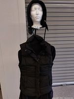 Black hooded padded vest displayed on head mannequin showing front view and hood.