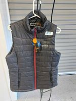 Front view of black Ororo padded heated vest hung on a white hanger showing embroidered Ororo logo and zipper detail.
