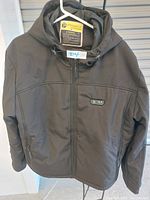 Front view of black Ptahdus heated jacket, showing hood, main zipper, and control panel buttons on chest