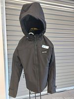 Black hooded heated jacket displayed on hanger showing front side and zipper.