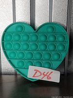 Photo of a teal heart-shaped silicone pop-it toy with rounded pop bubbles arranged in rows.