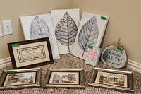 Overview of entire lot showing four framed prints, three leaf art panels, and two decorative signs arranged on carpet near wall.