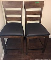 Two wooden bar stools side by side showing front view with padded seats and ladder backrest design