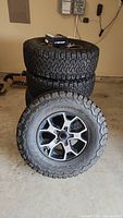 Five tires and wheels stacked in garage with TPMS sensor box on top.
