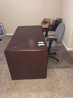 Side view of the large wooden desk and the grey rolling office chair positioned against a wall on carpeted floor.