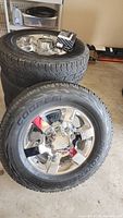 Four Cooper Discoverer AT tires mounted on GMC 8-lug chrome wheels with lug nuts on top tire.